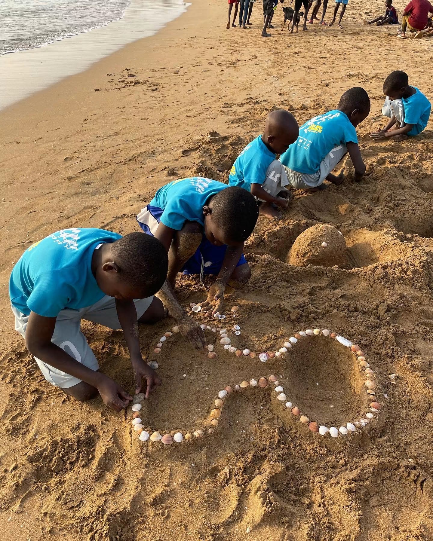 Enfants dessinant un cœur de coquillages dans le sable au bord de la mer
