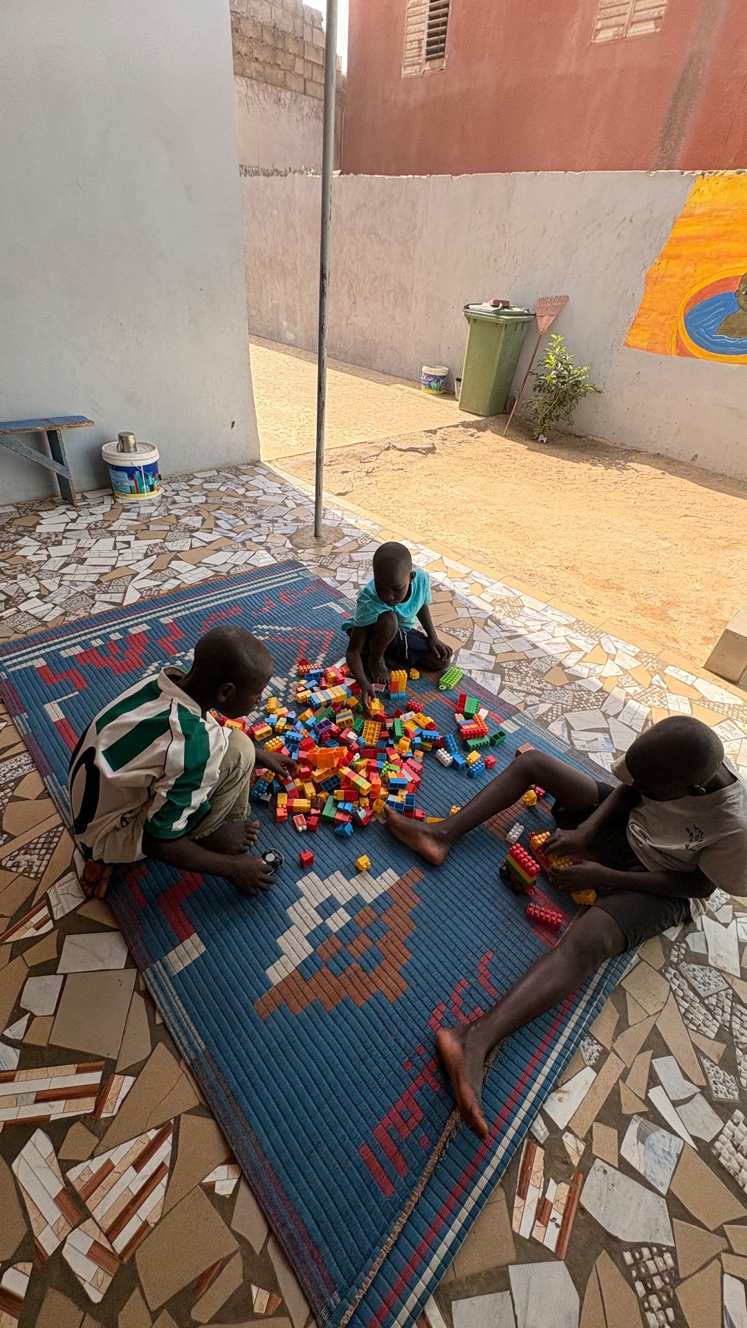 Trois enfants jouant avec des briques colorées sur une natte