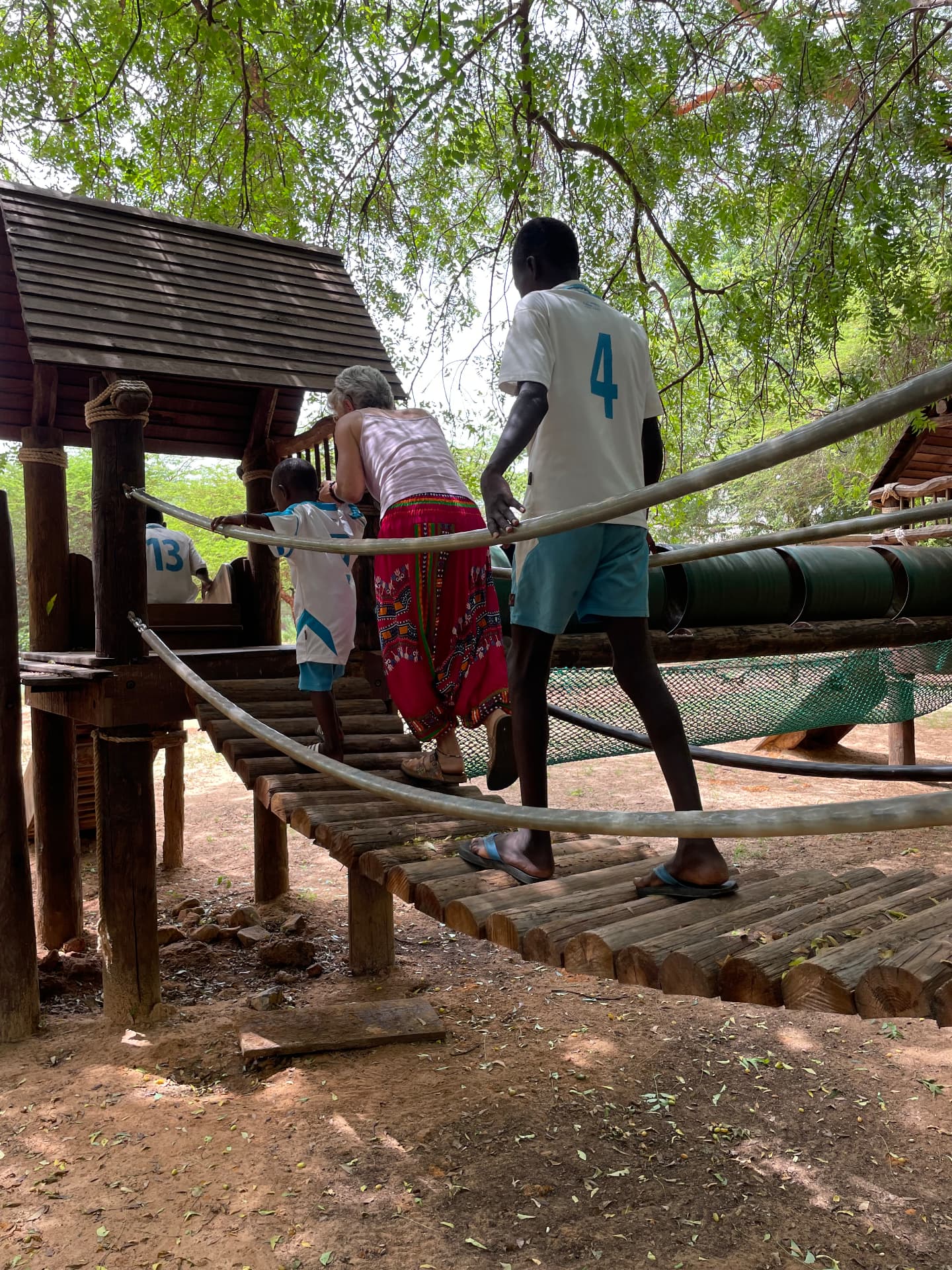 Enfant, adolescent et bénévole traversant un pont de singe en bois