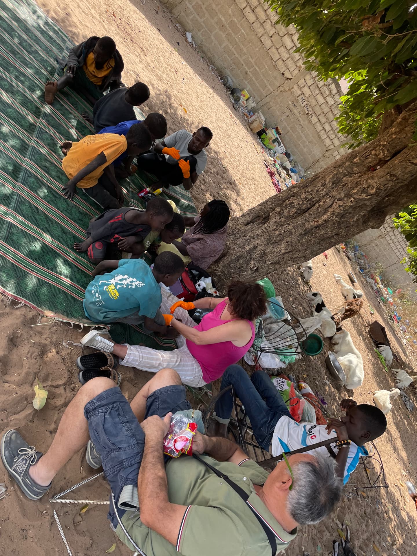 Bénévoles assis sur des nattes soignant des enfants talibés à l'extérieur