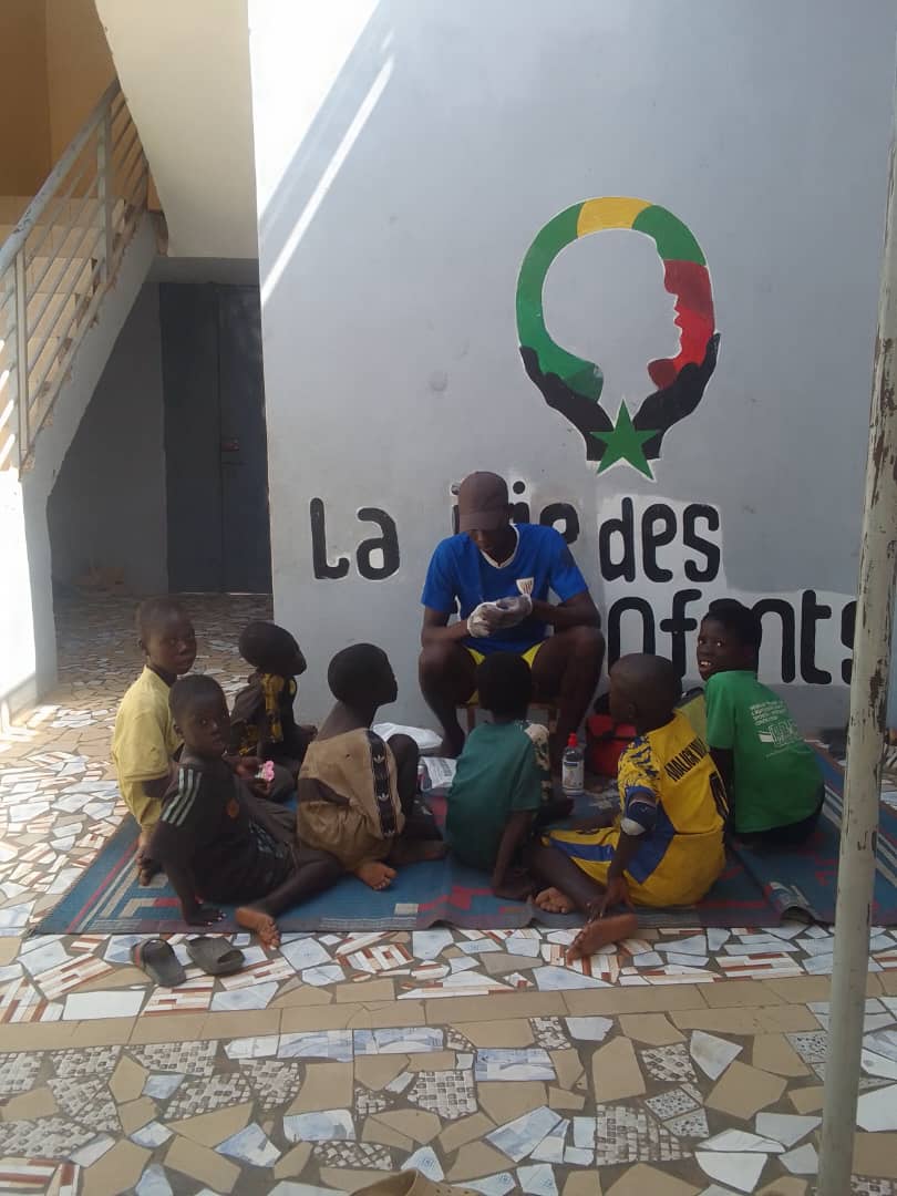 Enfants assis devant la fresque du logo La Joie des Enfants