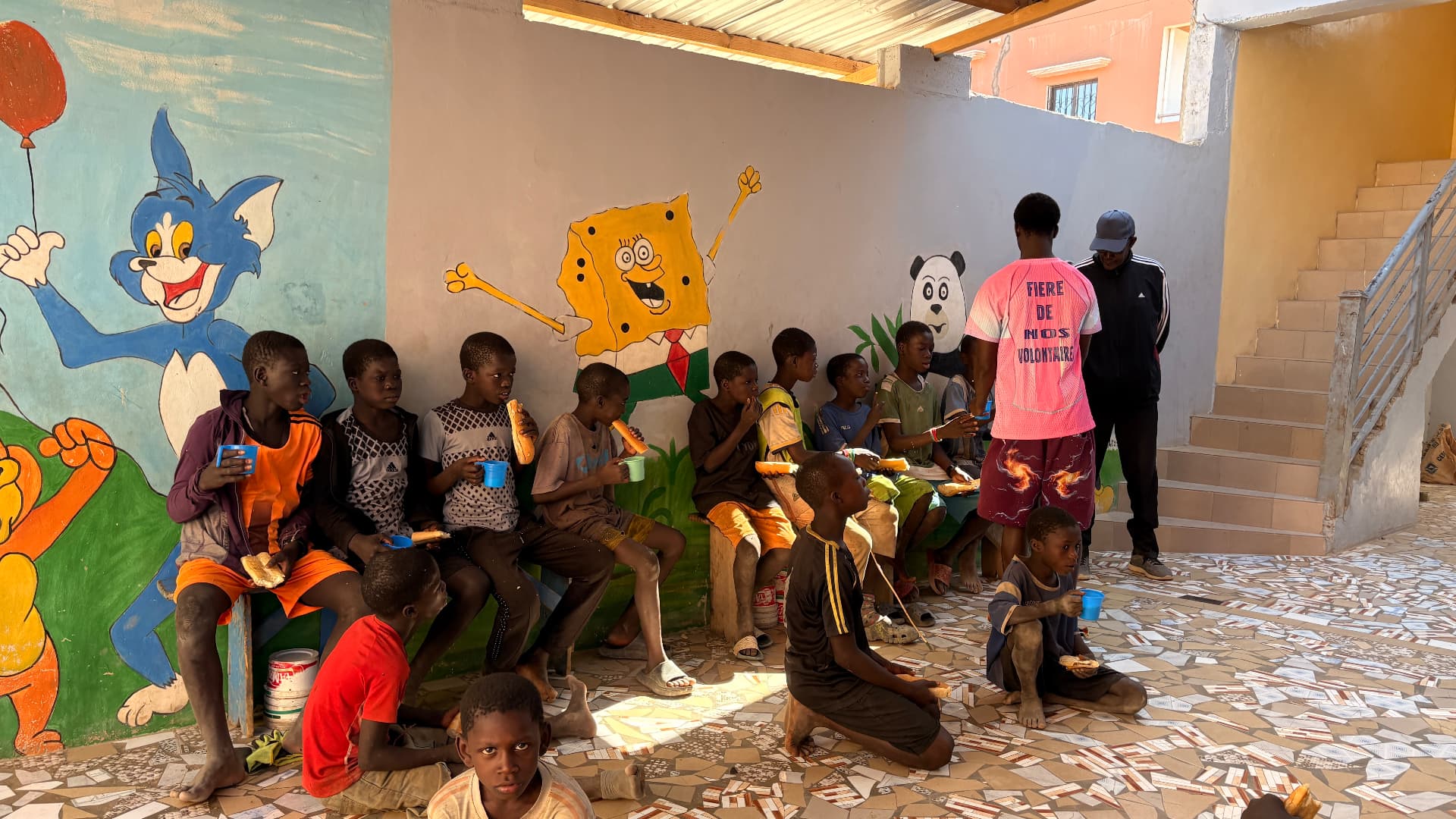 Enfants partageant un repas assis le long du mur peint du centre